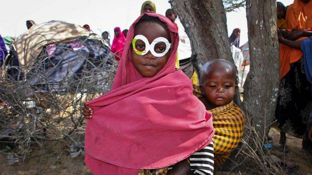 A young Somali girl displaced by drought wears mock spectacles cut from an antibiotics medicine box at a relief camp near the capital, Mogadishu, in March 2017. Photo: AP
