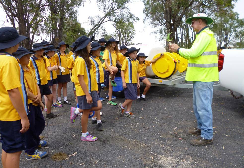 Project manager Brian Clancy shows the public school students how to handle the young trees. Pic: INVERELL TIMES
