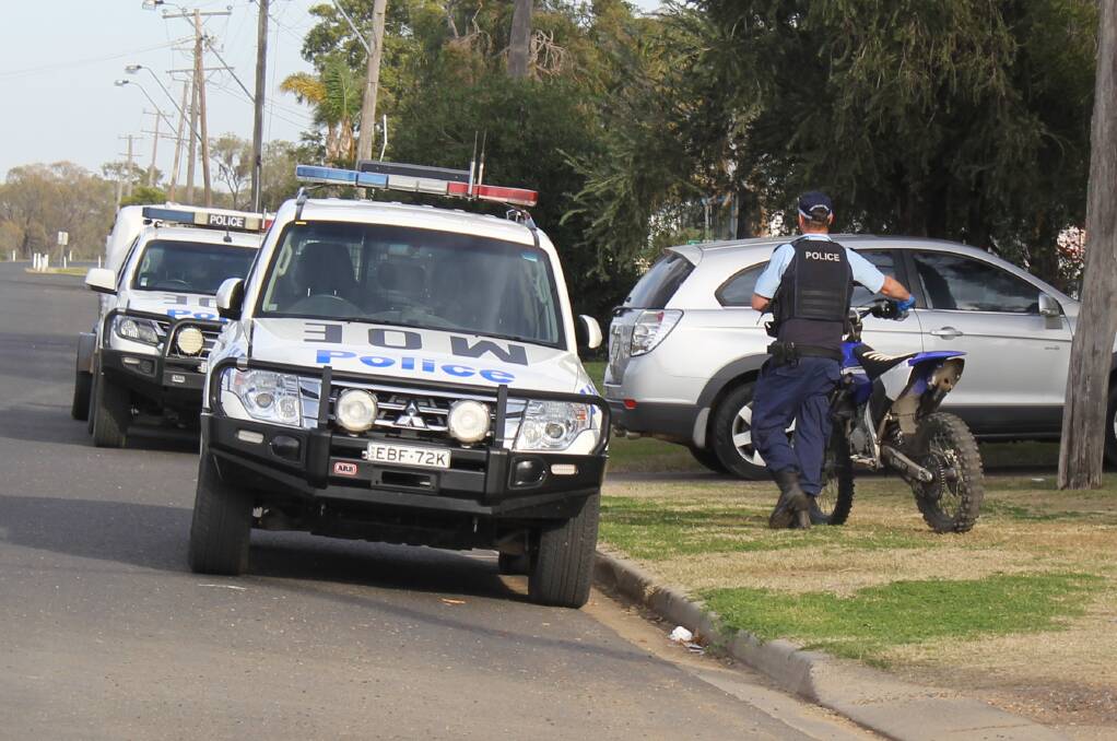 SEIZED: A police officer wheels away the blue Yamaha motorbike from an Anne Street address on Wednesday morning.