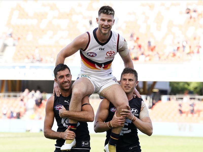 Bryce Gibbs is chaired off Metricon Stadium by former teamates Kade Simpson and Marc Murphy.